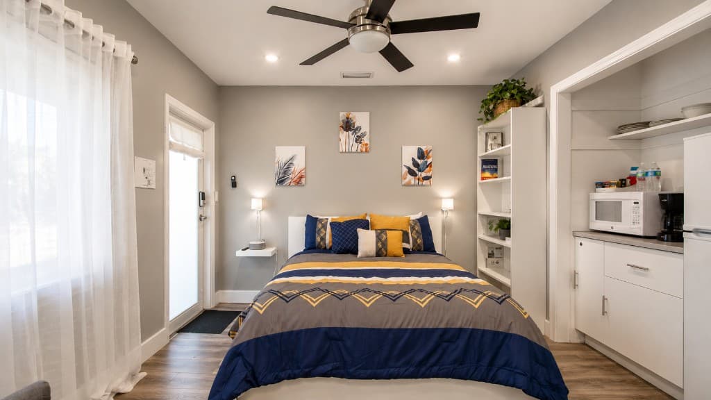 One-bedroom sleeping area with navy and gold bedding beside a compact kitchenette